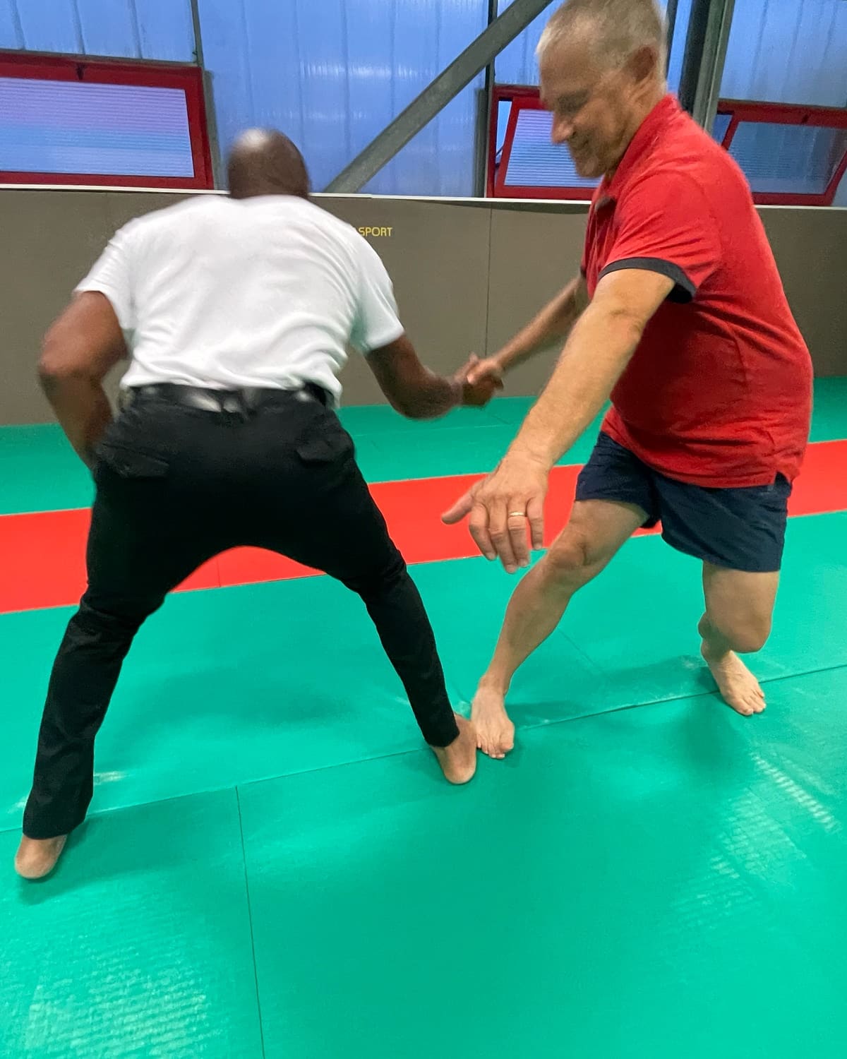 Exercice d’équilibre au cours seniors du Kobukaï à Séné : l’enseignant guide un participant par la main, pied contre pied sur le tatami